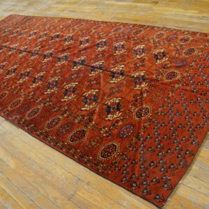 Rust colored rug with repeating geometric tribal designs covers a worn light wood floor.