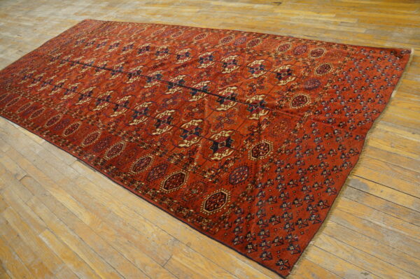 Rust colored rug with repeating geometric tribal designs covers a worn light wood floor.