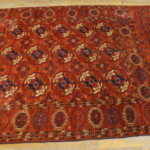 Red geometric rug with repeating dark blue and cream patterns laid on light wooden flooring.
