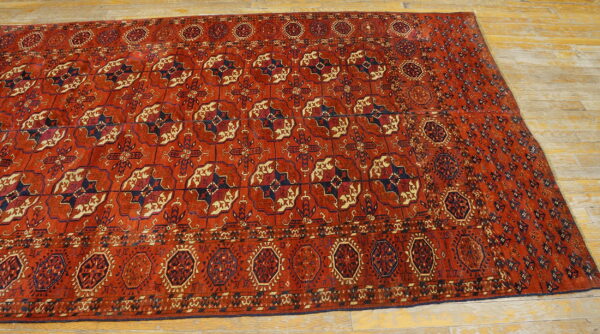 Red geometric rug with repeating dark blue and cream patterns laid on light wooden flooring.