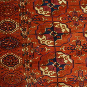 Low-pile rug in red and dark blue featuring angular geometric motifs next to light wood floorboards.