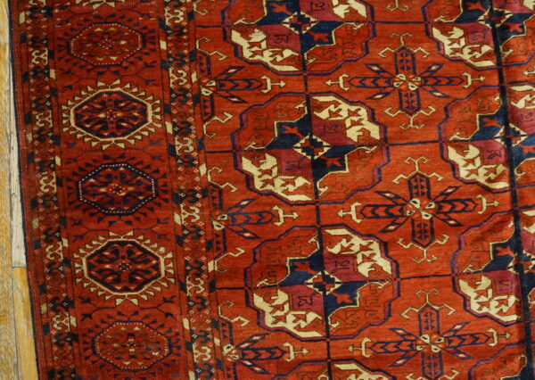 Low-pile rug in red and dark blue featuring angular geometric motifs next to light wood floorboards.