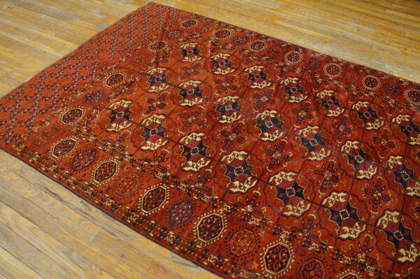 A rust-colored rug with repeating navy and cream geometric patterns rests on light hardwood plank flooring.
