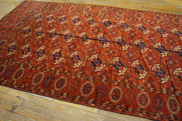 Red geometric rug with repeating navy and cream medallions fills the frame over light hardwood.