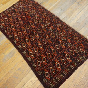 A runner featuring a geometric pattern in dark red and rust orange lies on light distressed wood planks.