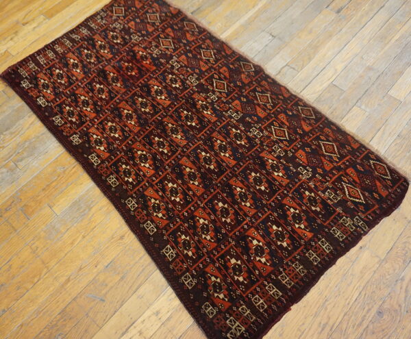 A runner featuring a geometric pattern in dark red and rust orange lies on light distressed wood planks.