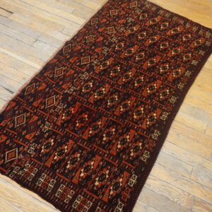 A low-pile rug with geometric patterns in deep red, brown, and blue rests on distressed wood flooring.
