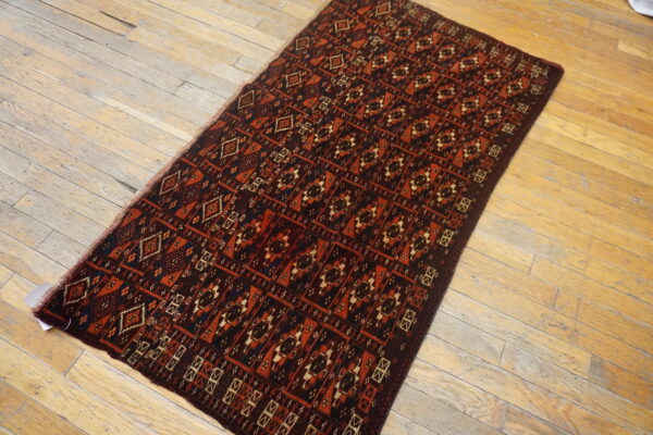 A low-pile rug with geometric patterns in deep red, brown, and blue rests on distressed wood flooring.