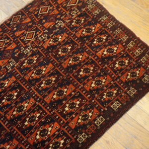 Burgundy rug with repetitive geometric patterns in deep red, navy, and tan on light wooden plank flooring.