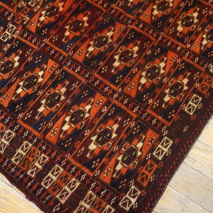 Traditional geometric rug with red, orange, dark blue, and cream colors on distressed wood floor.
