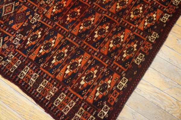 Traditional geometric rug with red, orange, dark blue, and cream colors on distressed wood floor.