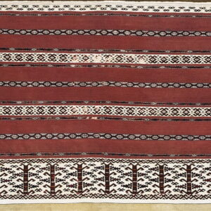 Close-up of a flatweave rug with wide maroon stripes and complex geometric bands in white and dark brown.
