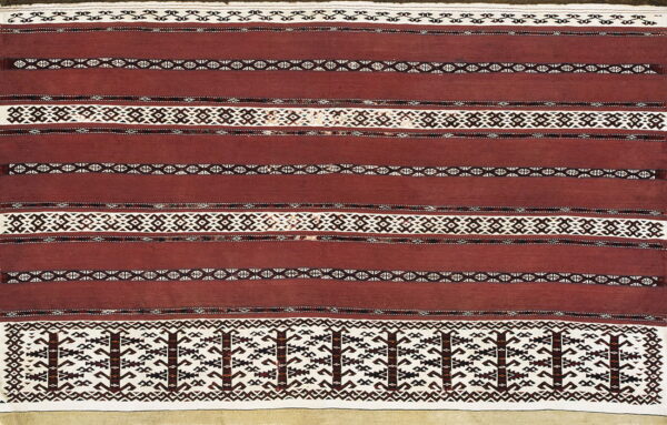Close-up of a flatweave rug with wide maroon stripes and complex geometric bands in white and dark brown.