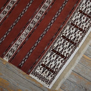 Terracotta and cream flat weave rug with geometric striped patterns resting on weathered gray wood planks.