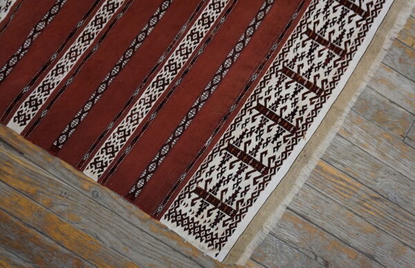 Terracotta and cream flat weave rug with geometric striped patterns resting on weathered gray wood planks.