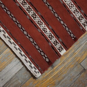 Red-brown, white, and dark striped flatweave rug displaying geometric patterns rests on rustic wooden planks.
