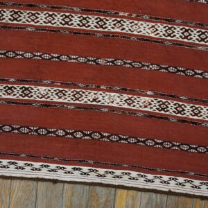 Rust flatweave rug featuring horizontal stripes with geometric white and dark brown patterns on wood flooring.