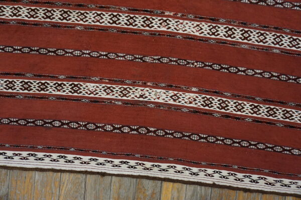 Rust flatweave rug featuring horizontal stripes with geometric white and dark brown patterns on wood flooring.