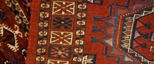 Geometric rug detail showing repeating medallions and angular motifs in red, navy, blue, and cream.