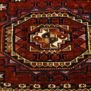 Deep red geometric rug detail showing a complex octagonal medallion with navy, cream, and pink patterns.