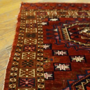 Geometric red and blue rug displaying a detailed medallion and borders resting on aged wooden floorboards.