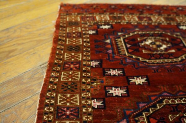 Geometric red and blue rug displaying a detailed medallion and borders resting on aged wooden floorboards.