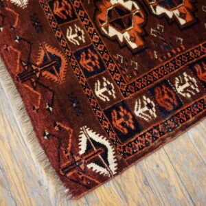 Deep red rug with orange, white, and dark blue geometric patterns resting on distressed wood flooring.