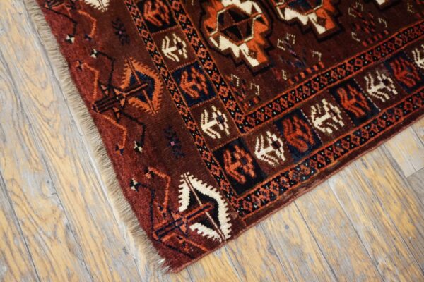 Deep red rug with orange, white, and dark blue geometric patterns resting on distressed wood flooring.