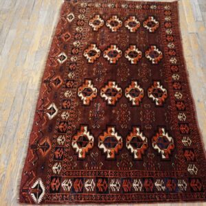 Traditional low-pile rug in deep red, orange, and navy geometric patterns on distressed wood planks.