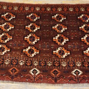 Dark red-brown high-pile rug displays repeating geometric medallions and detailed borders on light wood floor.