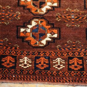 Traditional rug detail showing maroon, rust orange, cream, and navy geometric designs on wood flooring.