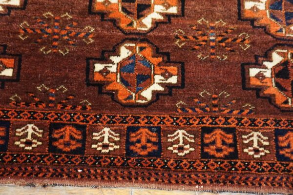 Traditional rug detail showing maroon, rust orange, cream, and navy geometric designs on wood flooring.