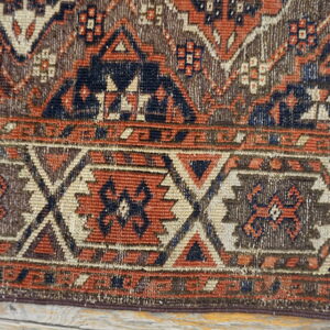 Close-up of a low-pile rug border featuring geometric patterns in navy, rust, brown, and cream.
