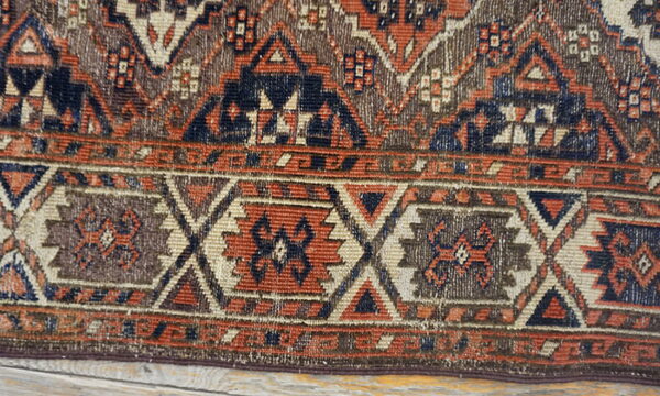 Close-up of a low-pile rug border featuring geometric patterns in navy, rust, brown, and cream.