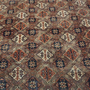 Geometric rug with rust and navy diamond motifs on a gray field, resting on light flooring.