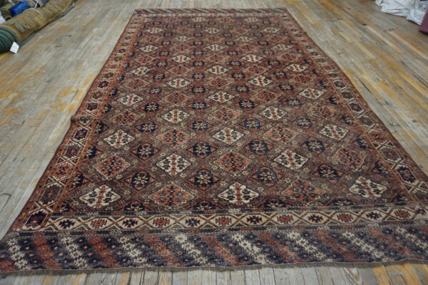 Rectangular rug featuring repeating geometric diamonds in muted brown, rust, and navy blue on a wood floor.