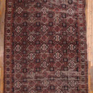 Distressed geometric rug in dark brown, terracotta, and cream, displayed on light wood flooring.
