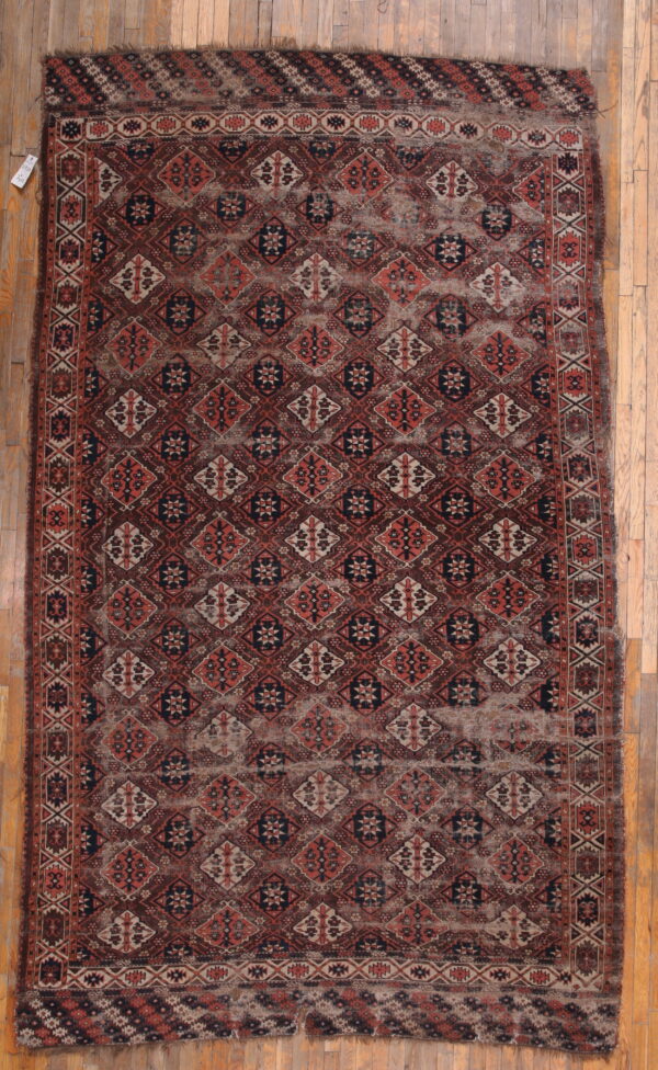Distressed geometric rug in dark brown, terracotta, and cream, displayed on light wood flooring.