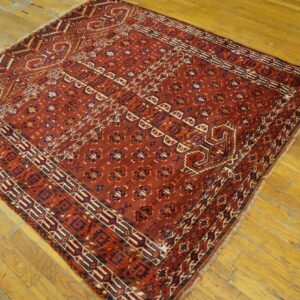 Deep red geometric rug with blue and cream accents displayed on distressed wood planks.