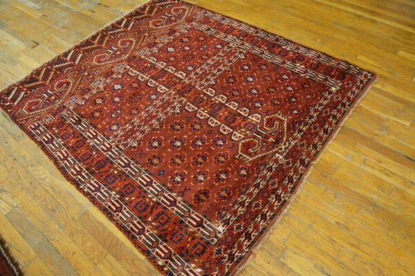 Deep red geometric rug with blue and cream accents displayed on distressed wood planks.