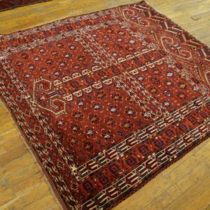 A deep red geometric patterned rug with navy and cream accents rests on worn wooden floors.