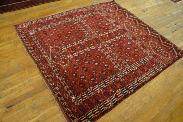 A deep red geometric patterned rug with navy and cream accents rests on worn wooden floors.