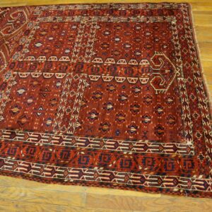 A deep red geometric tribal rug with navy and cream details lies on worn golden hardwood floor.