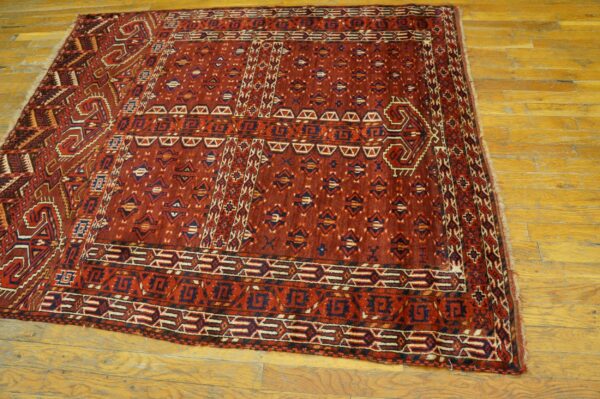 A deep red geometric tribal rug with navy and cream details lies on worn golden hardwood floor.