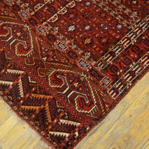 Deep red geometric rug featuring navy and cream motifs rests on bright yellow wooden plank flooring.