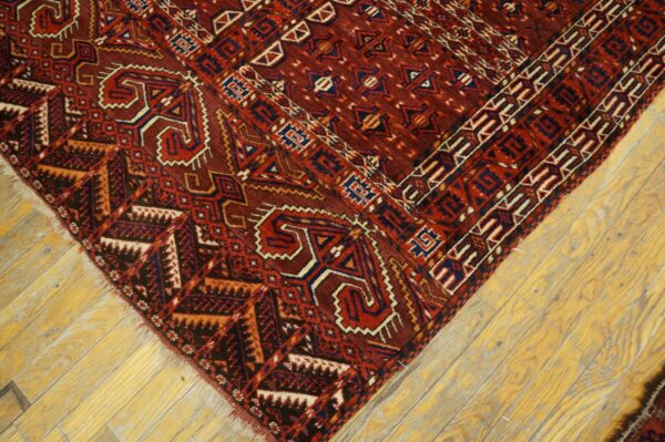 Deep red geometric rug featuring navy and cream motifs rests on bright yellow wooden plank flooring.