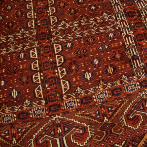 Densely patterned rug in deep red, blue, and cream colors rests on light wooden floorboards.