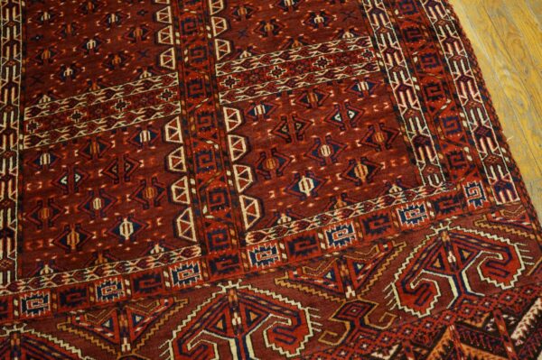 Densely patterned rug in deep red, blue, and cream colors rests on light wooden floorboards.