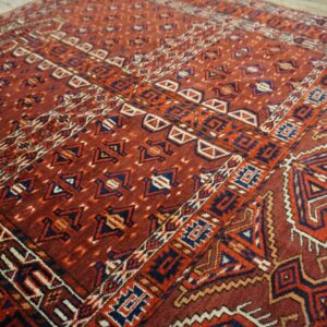 Red geometric patterned rug featuring navy blue, orange, and cream accents on rustic wood flooring.
