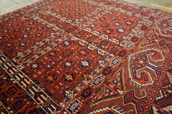 Red geometric patterned rug featuring navy blue, orange, and cream accents on rustic wood flooring.